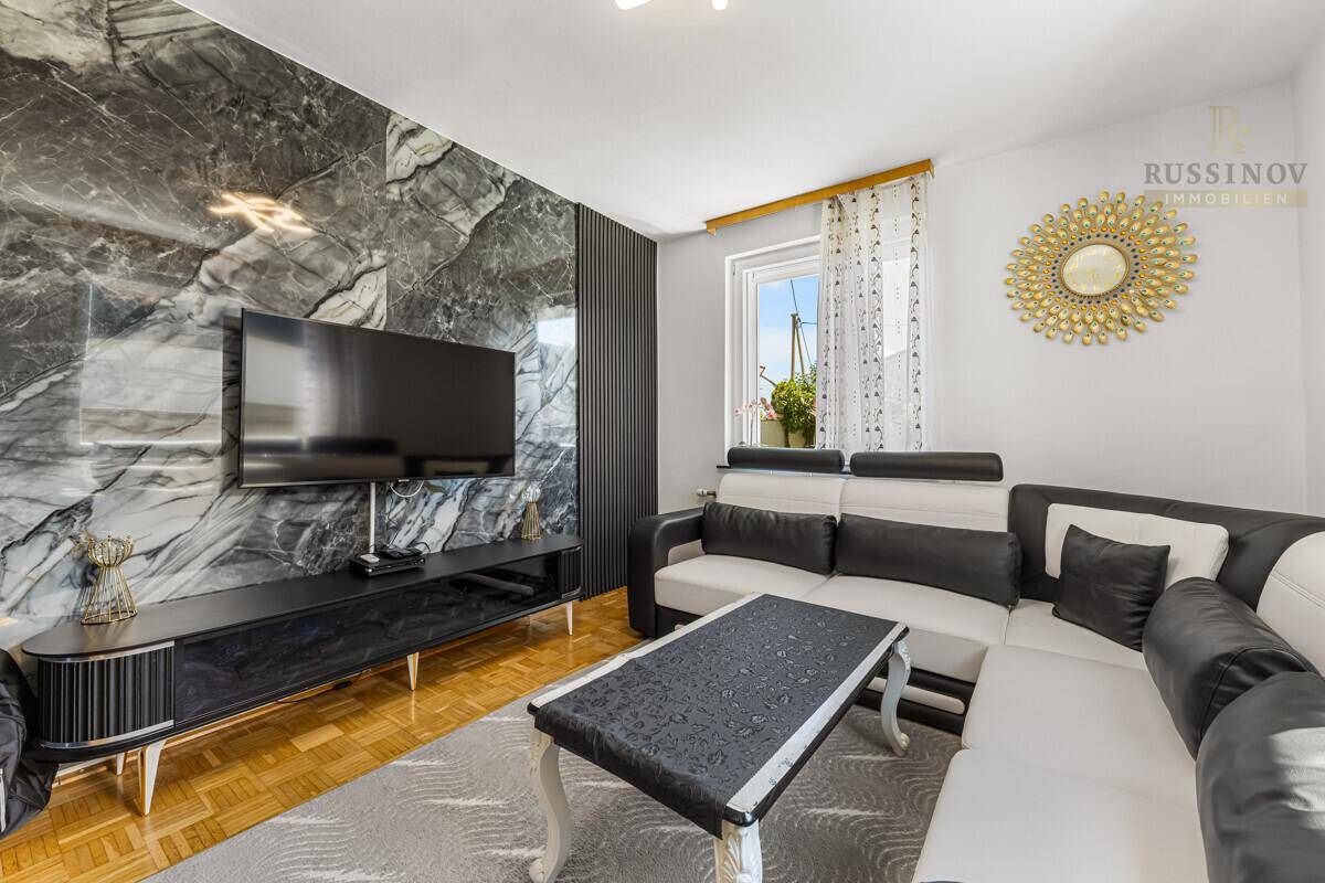 Gemütliches Wohnzimmer mit Ecksofa, dunkler Marmorwand und Parkettboden.