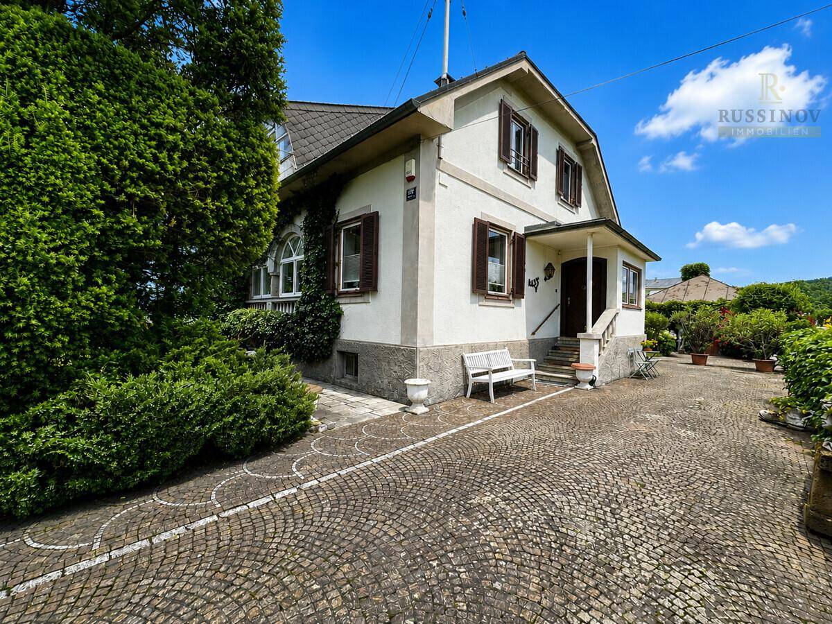Freistehendes Haus mit gepflasterter Auffahrt und Sitzbank im Vorgarten unter blauem Himmel.