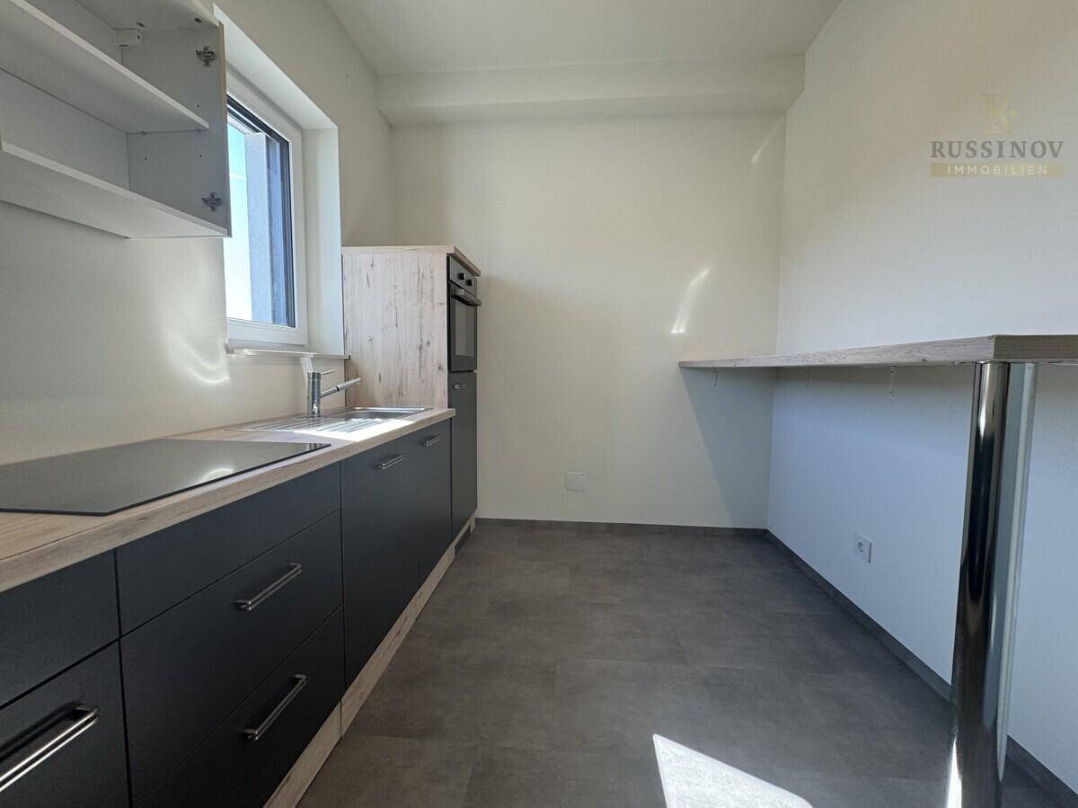 Moderne Küchenzeile mit dunklen Schränken, Holzarbeitsplatte und Fenster.