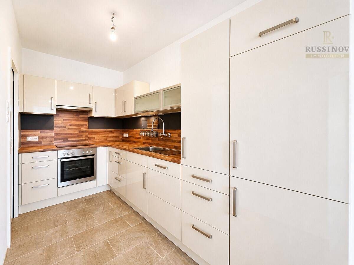 Helle Einbauküche mit weißen Schränken, Holzdetails und Fliesenboden.