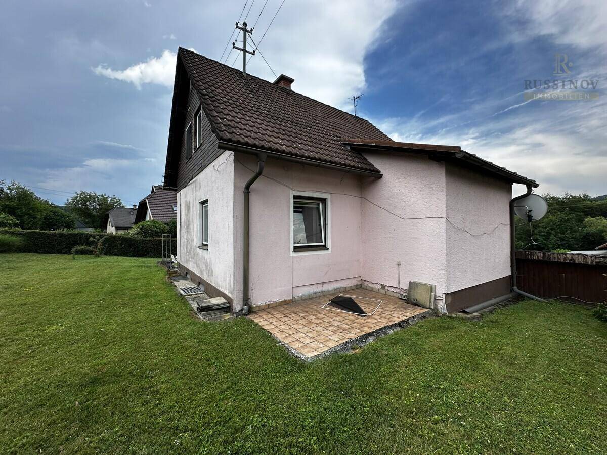 Seitenansicht des Hauses mit einer kleinen gepflasterten Fläche und Rasen.