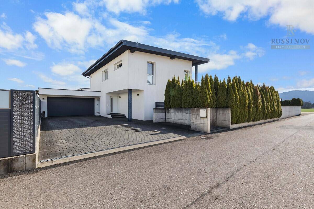 Modernes Einfamilienhaus mit Doppelgarage, gepflasterter Auffahrt und gepflegter Hecke.