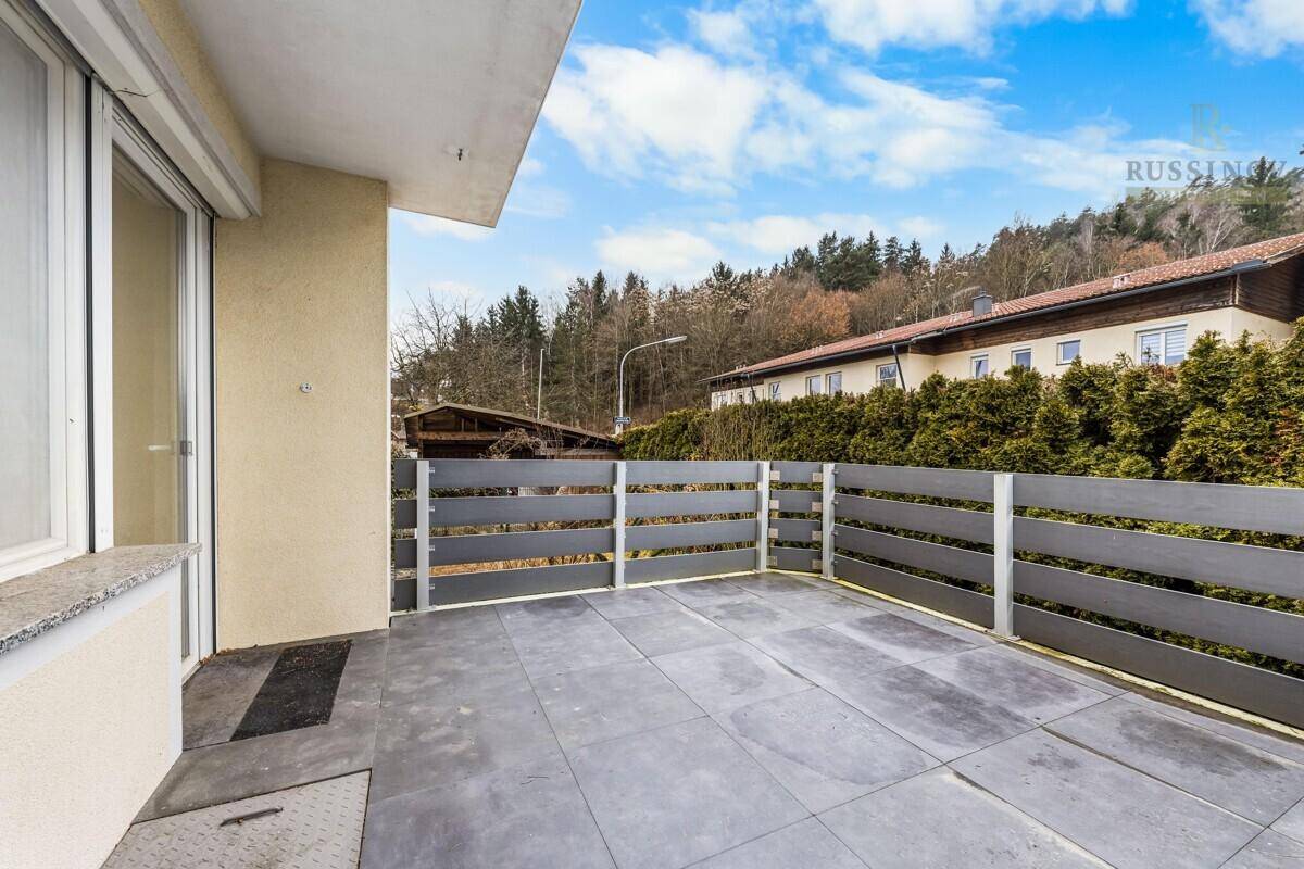 Geräumige Terrasse mit modernen Fliesen, Holzzaun und Blick ins Grüne unter blauem Himmel.