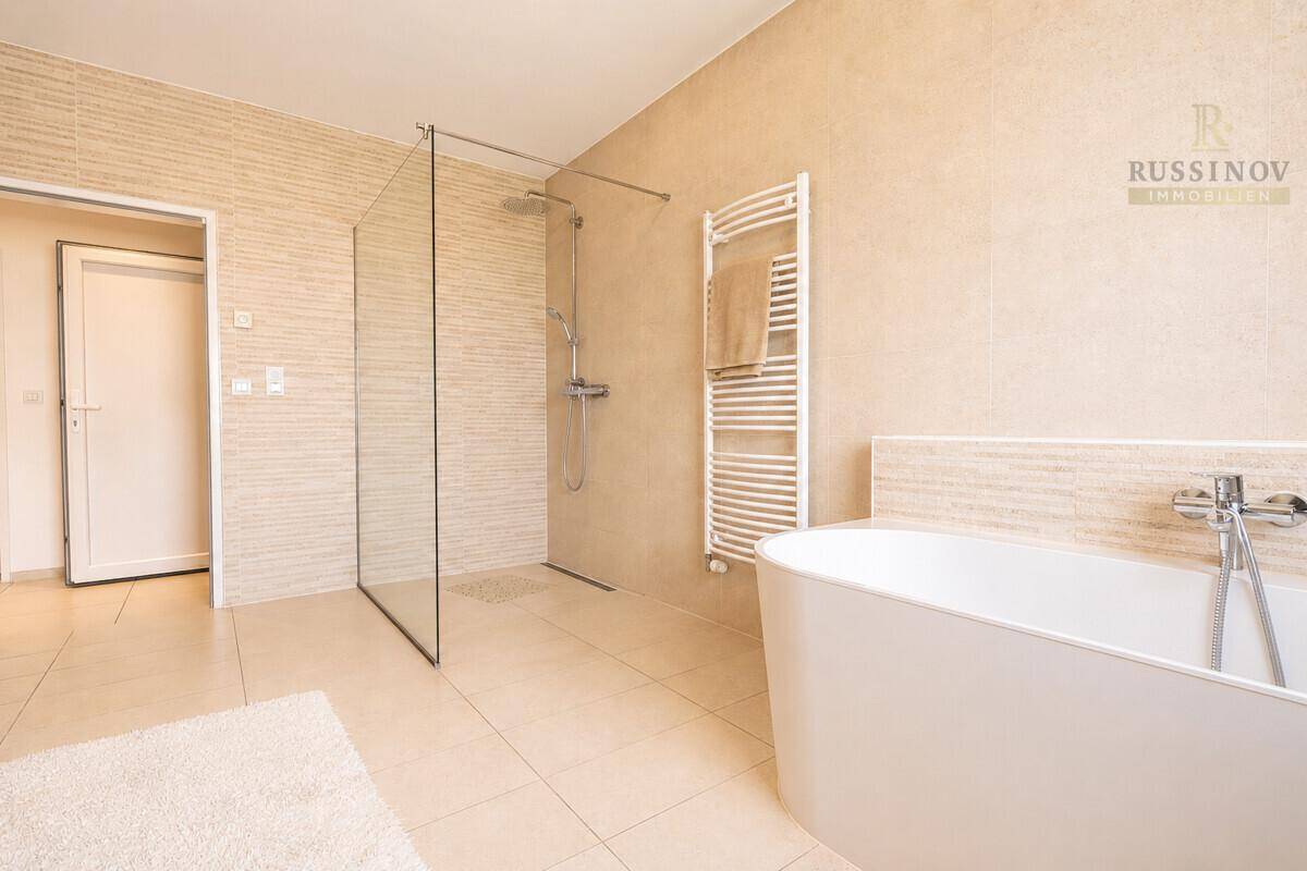 Modernes Badezimmer mit freistehender Badewanne, großer begehbarer Dusche und beigen Fliesen.