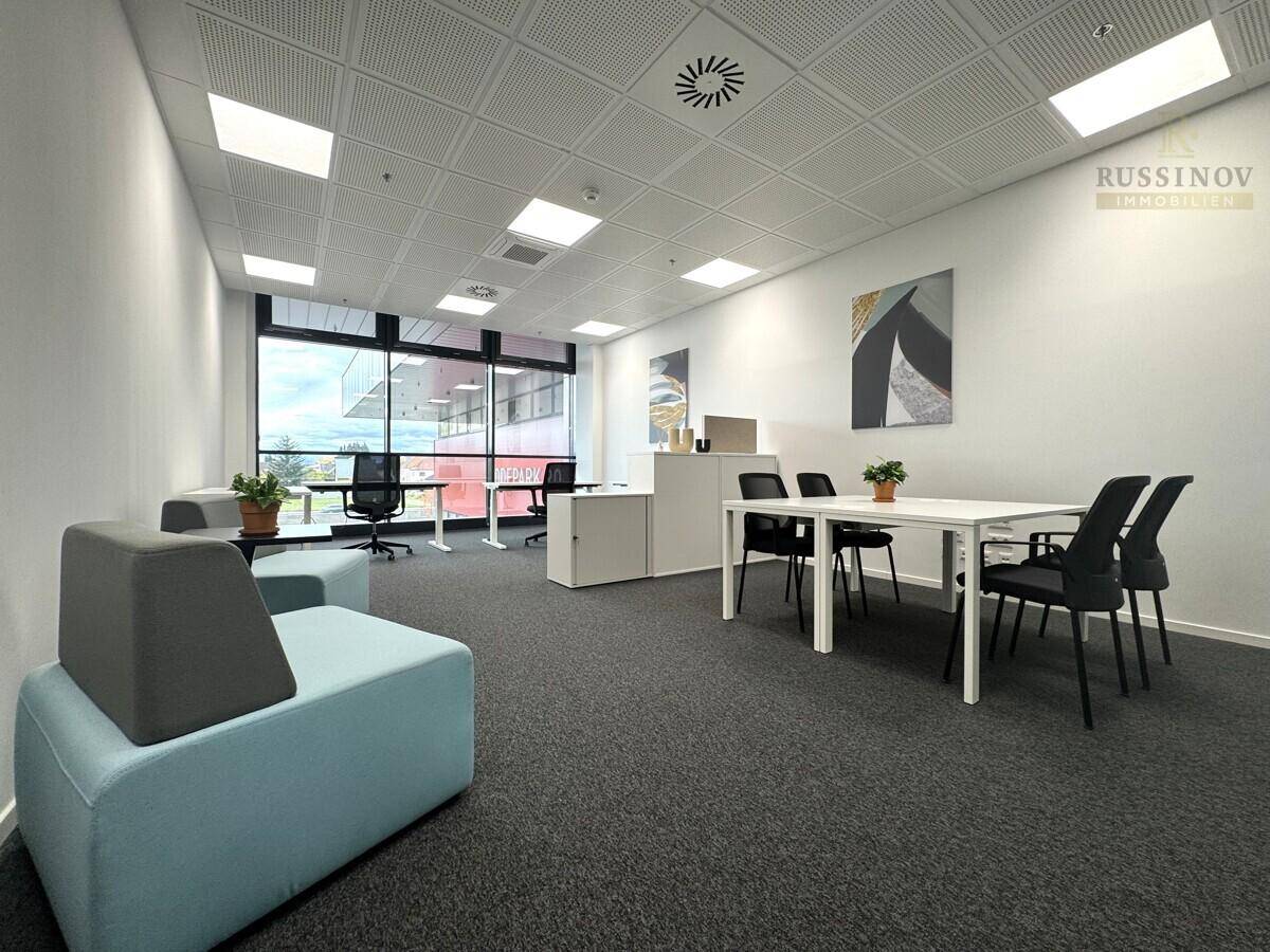 Modernes Büro mit flexiblen Arbeitsbereichen, großen Fenstern und einem Besprechungstisch.