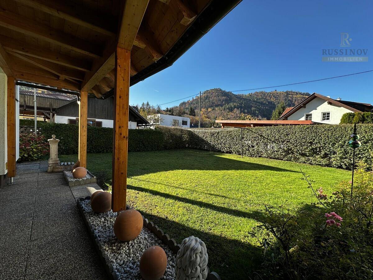 Sonnige Rasenfläche mit überdachtem Sitzbereich und Blick auf die umliegende Berglandschaft.