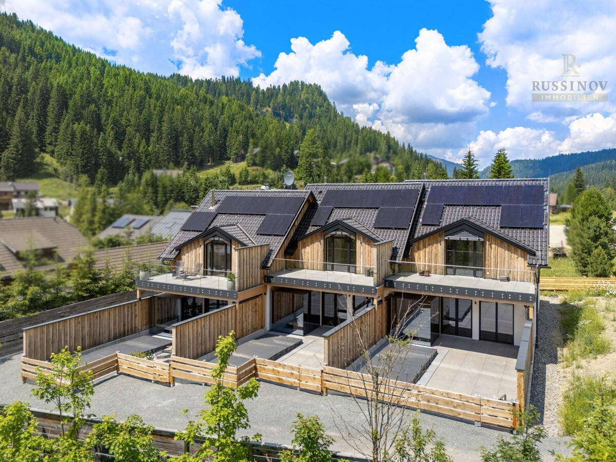 Moderne Chalets mit Holzfassaden, Solaranlagen auf den Dächern und privaten Terrassenbereichen in den Bergen.