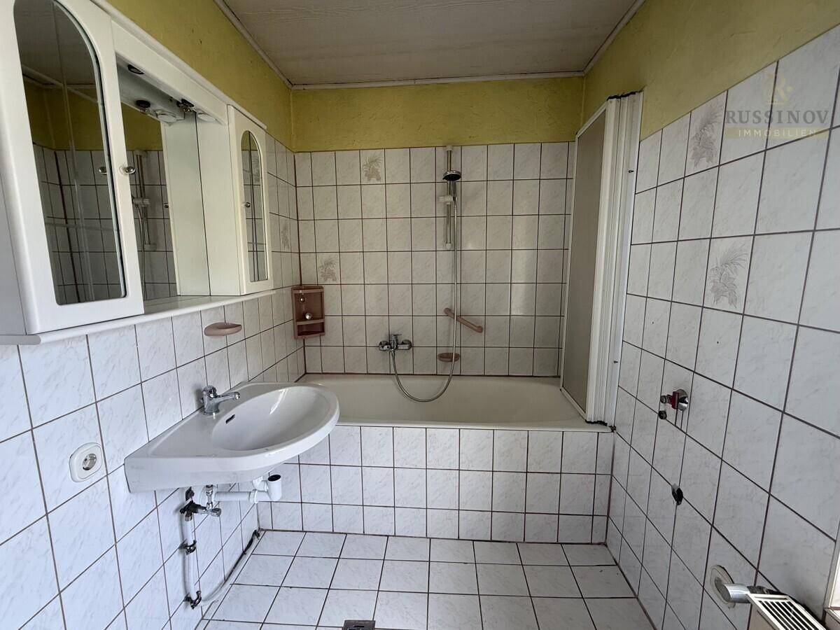 Badezimmer mit weißen Fliesen, Badewanne mit Duschvorhang und einem Waschbecken mit Spiegelschrank.