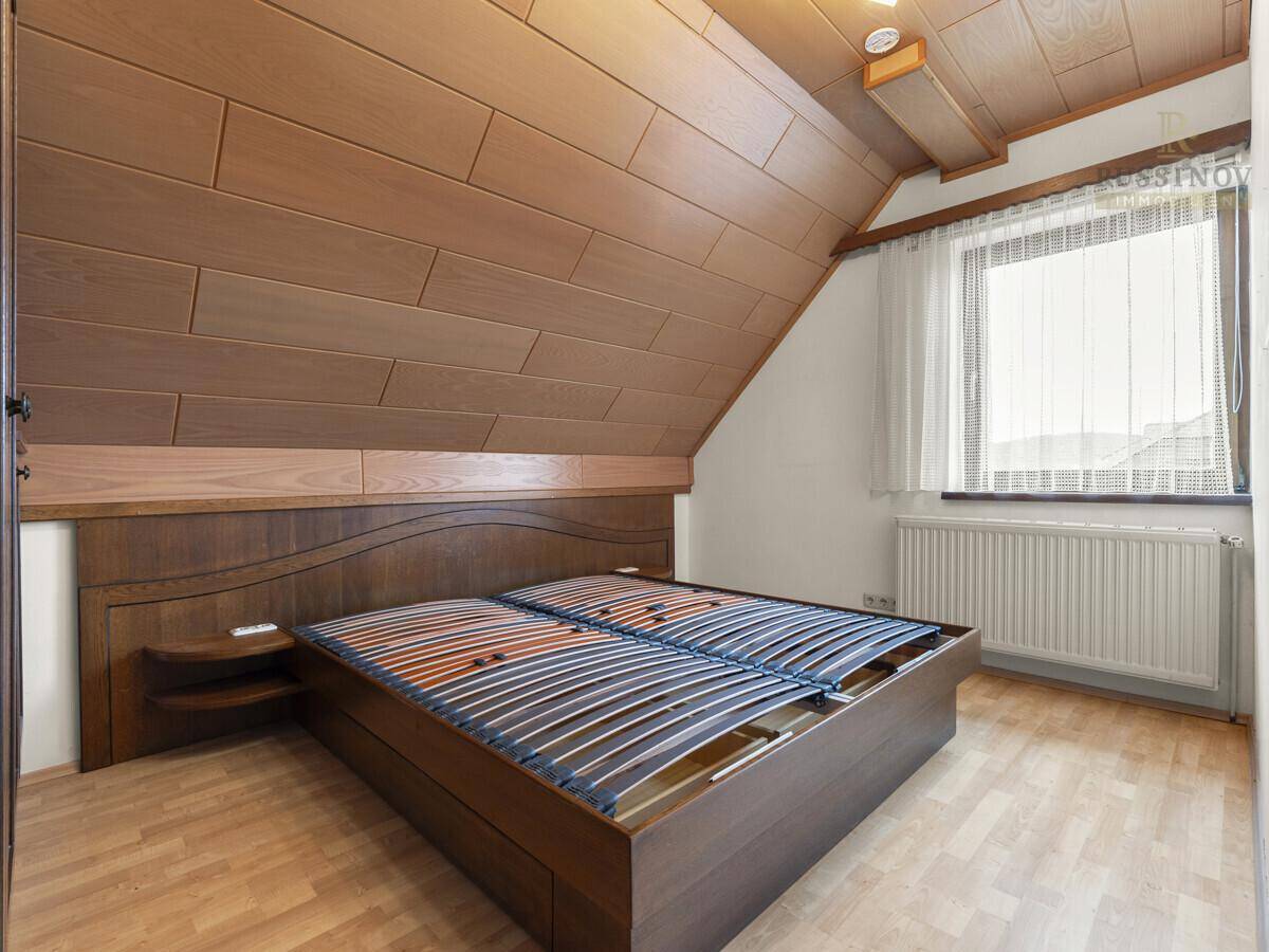Schlafzimmer mit Holzbettrahmen, Laminatboden und Dachschräge.