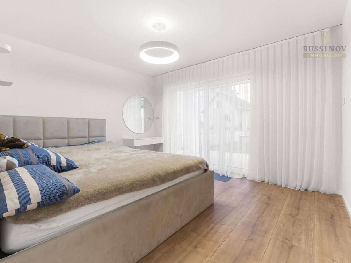 Helles Schlafzimmer mit Holzboden, großem Bett und Zugang zu einem Außenbereich.