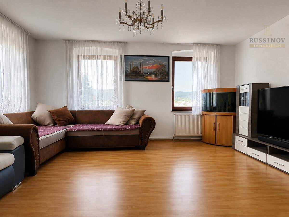 Geräumiges Wohnzimmer mit großem Ecksofa, Kronleuchter und hellen Fenstern.