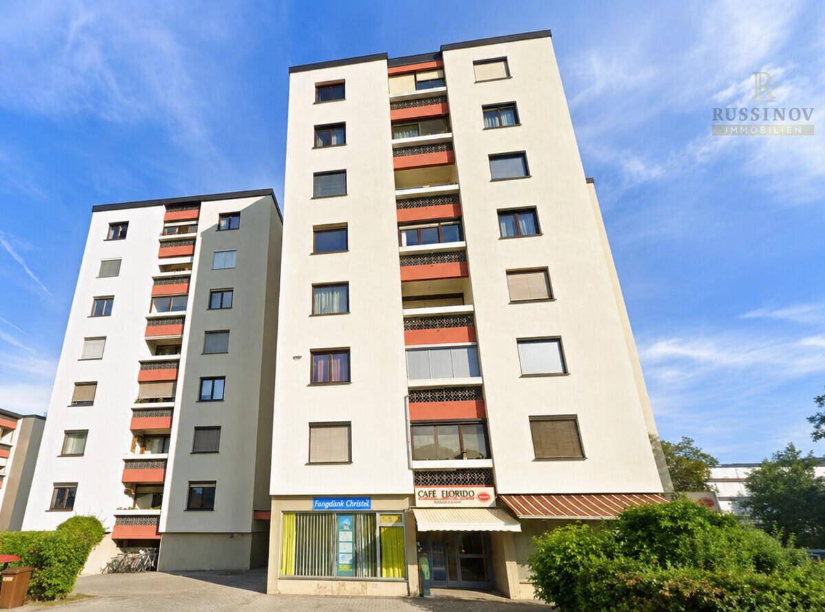 Modernes Mehrfamilienhaus mit mehreren Etagen, Balkonen und Geschäften im Erdgeschoss.
