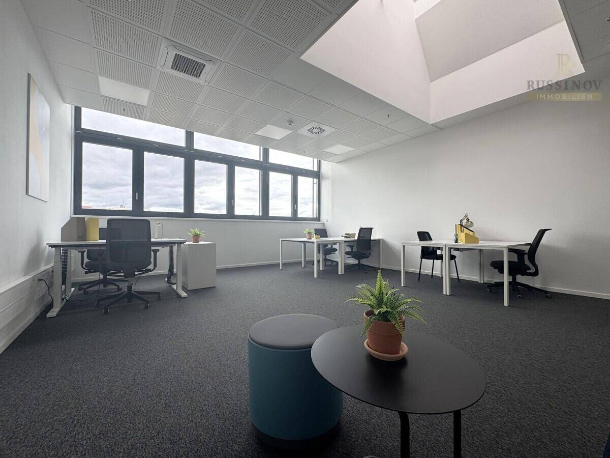 Geräumiges und helles Büro mit großen Fenstern, mehreren Arbeitsplätzen und Teppichboden.