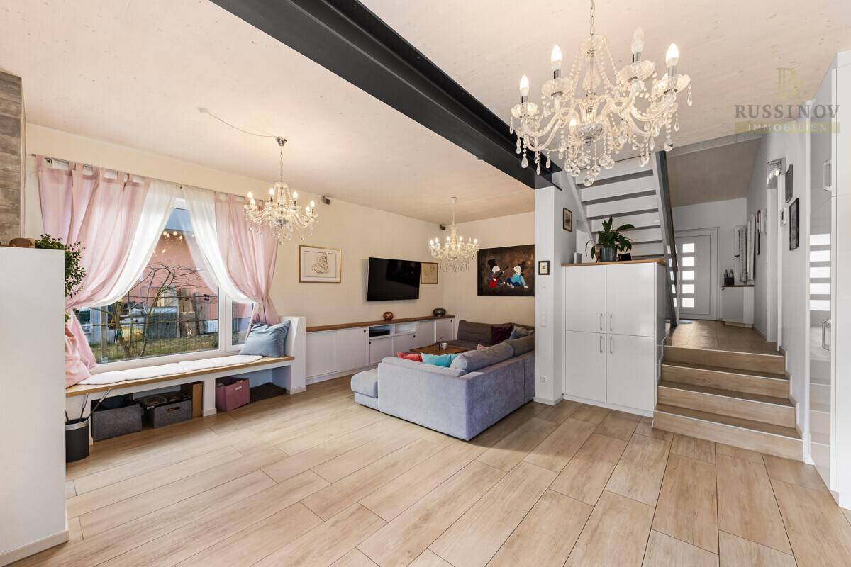 Helles Wohnzimmer mit Parkettboden, gemütlicher Sitzecke am Fenster und eleganten Kronleuchtern.