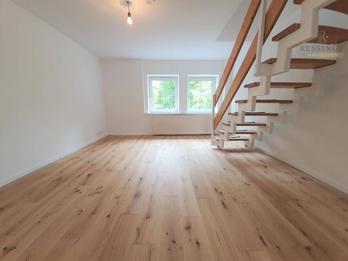 Heller Wohnbereich mit hochwertigem Holzdielenboden, großen Fenstern und einer eleganten Holztreppe.