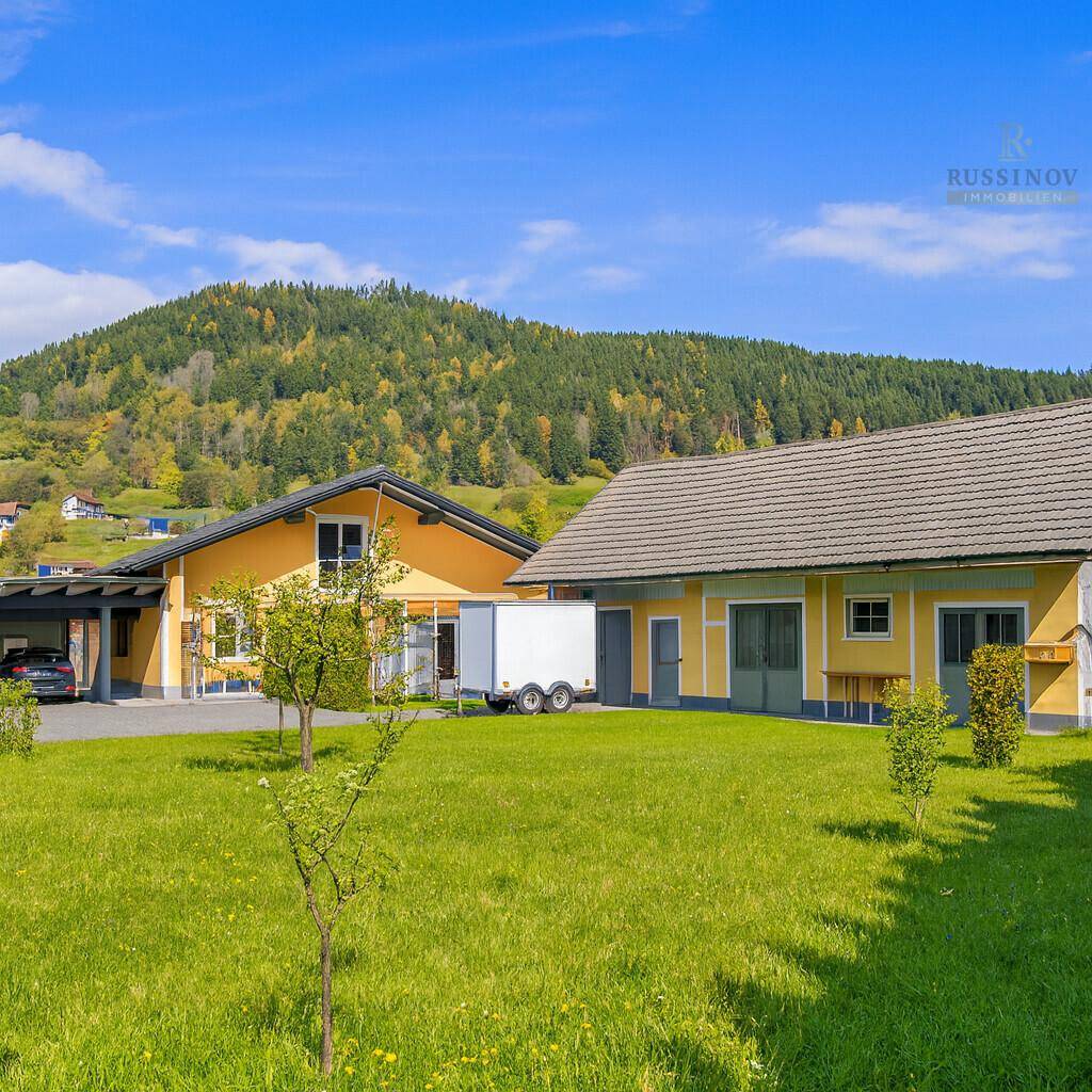 Weitläufiger Gartenbereich mit zwei Gebäuden und grüner Wiese unter blauem Himmel.