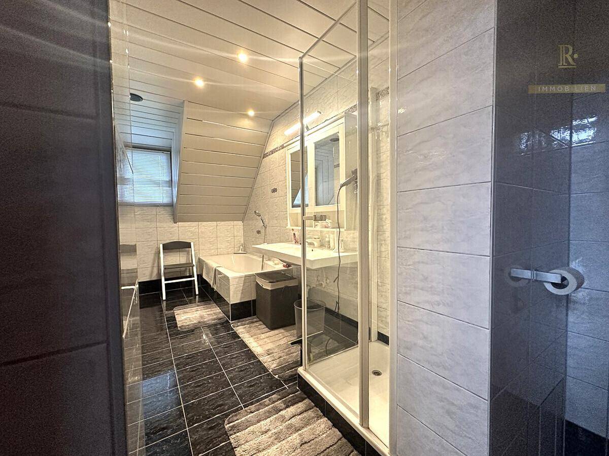 Modernes Badezimmer mit Dusche, Badewanne und Dachschräge, ausgestattet mit grauen und schwarzen Fliesen.