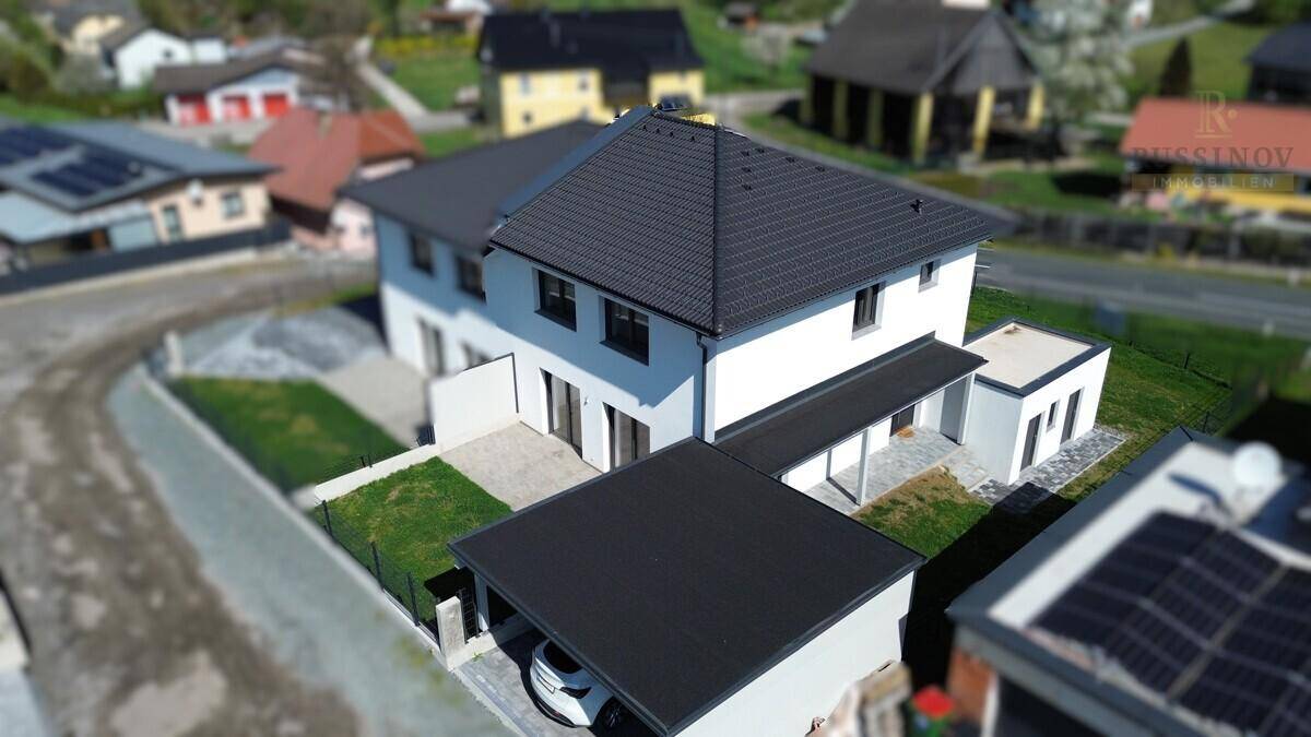Moderne Einfamilienhaus-Architektur mit dunklem Dach und Carport in einer Wohnsiedlung.