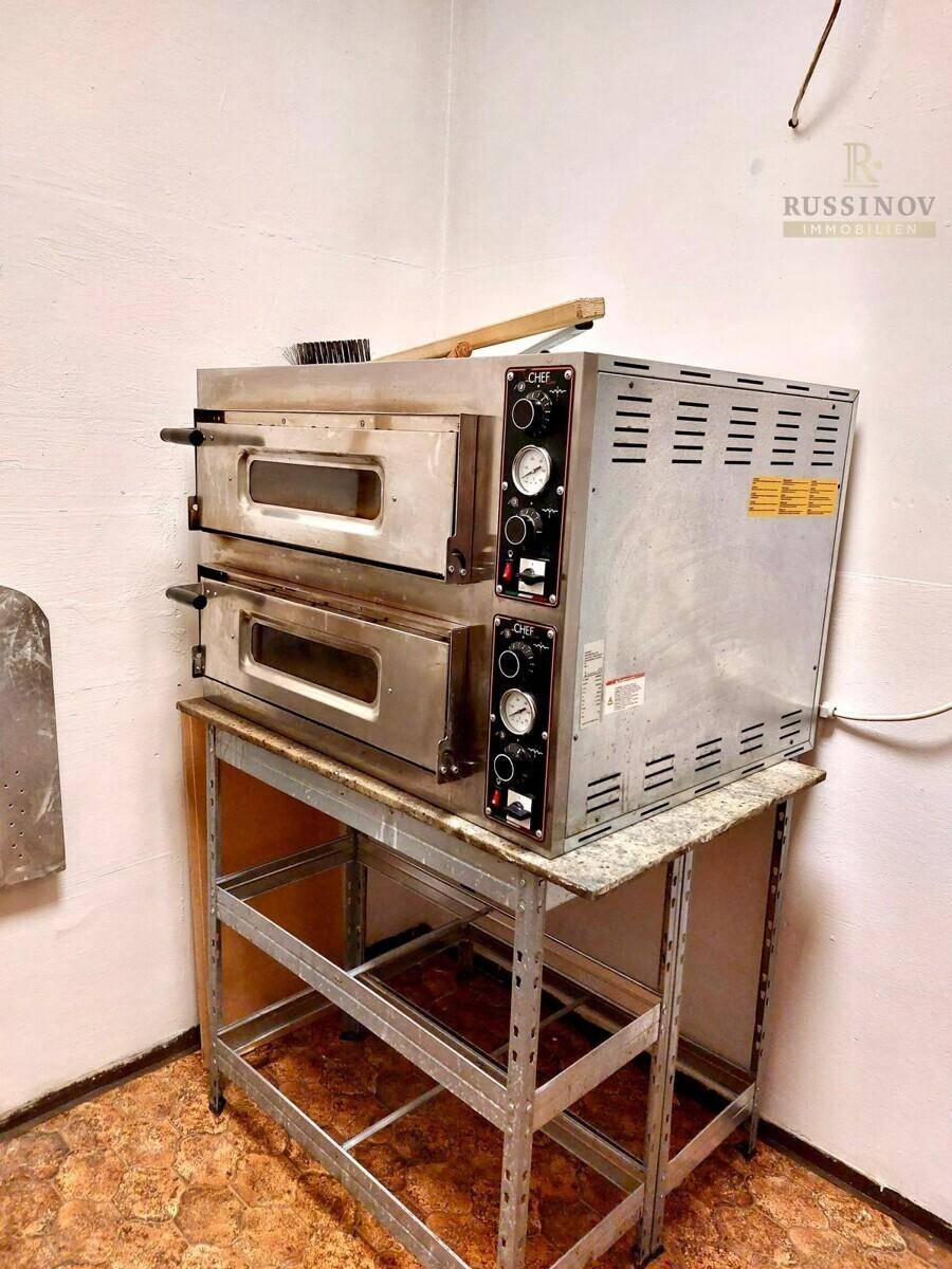 Zwei professionelle Pizzaöfen auf einem Metallgestell in einer gewerblichen Küche.