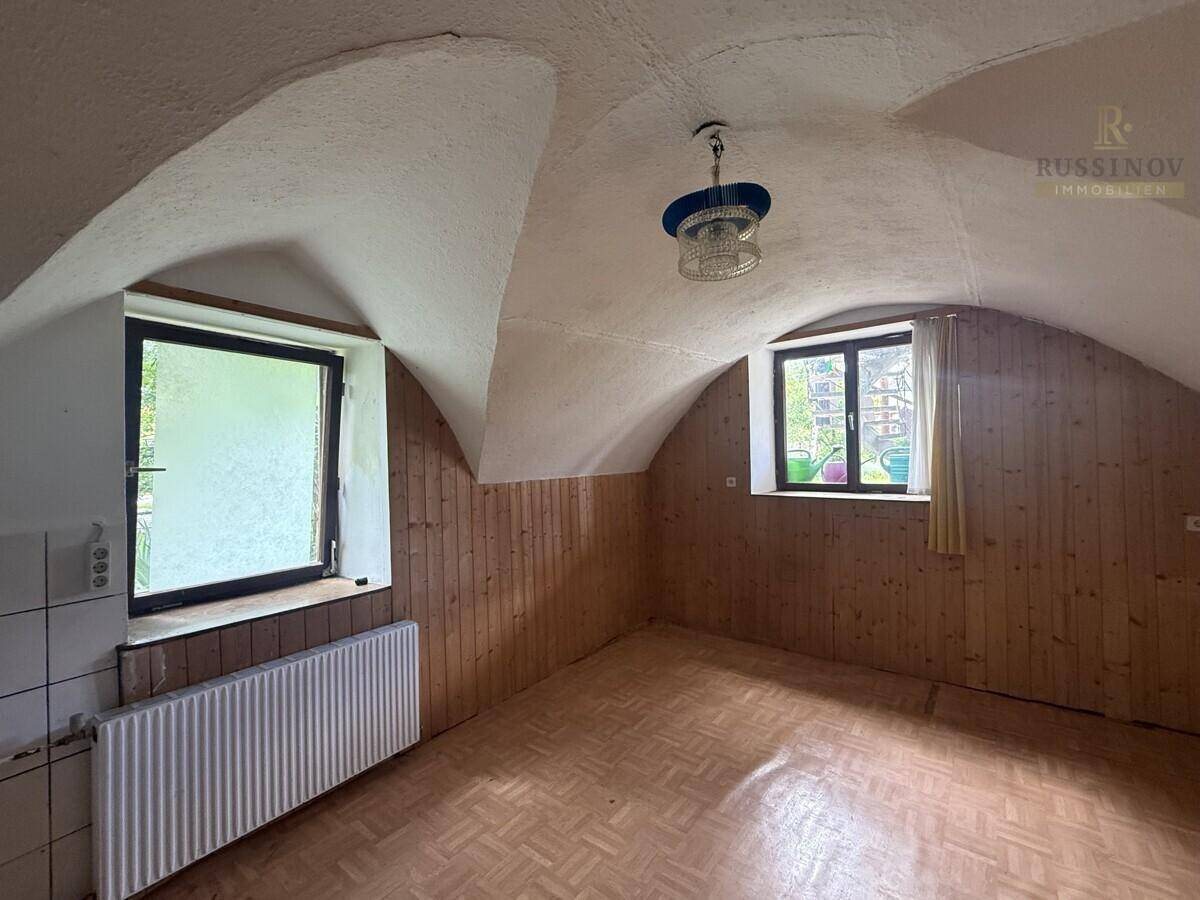 Raum mit Gewölbedecke, Holzvertäfelung und Parkettboden, ausgestattet mit zwei Fenstern und einem Heizkörper.