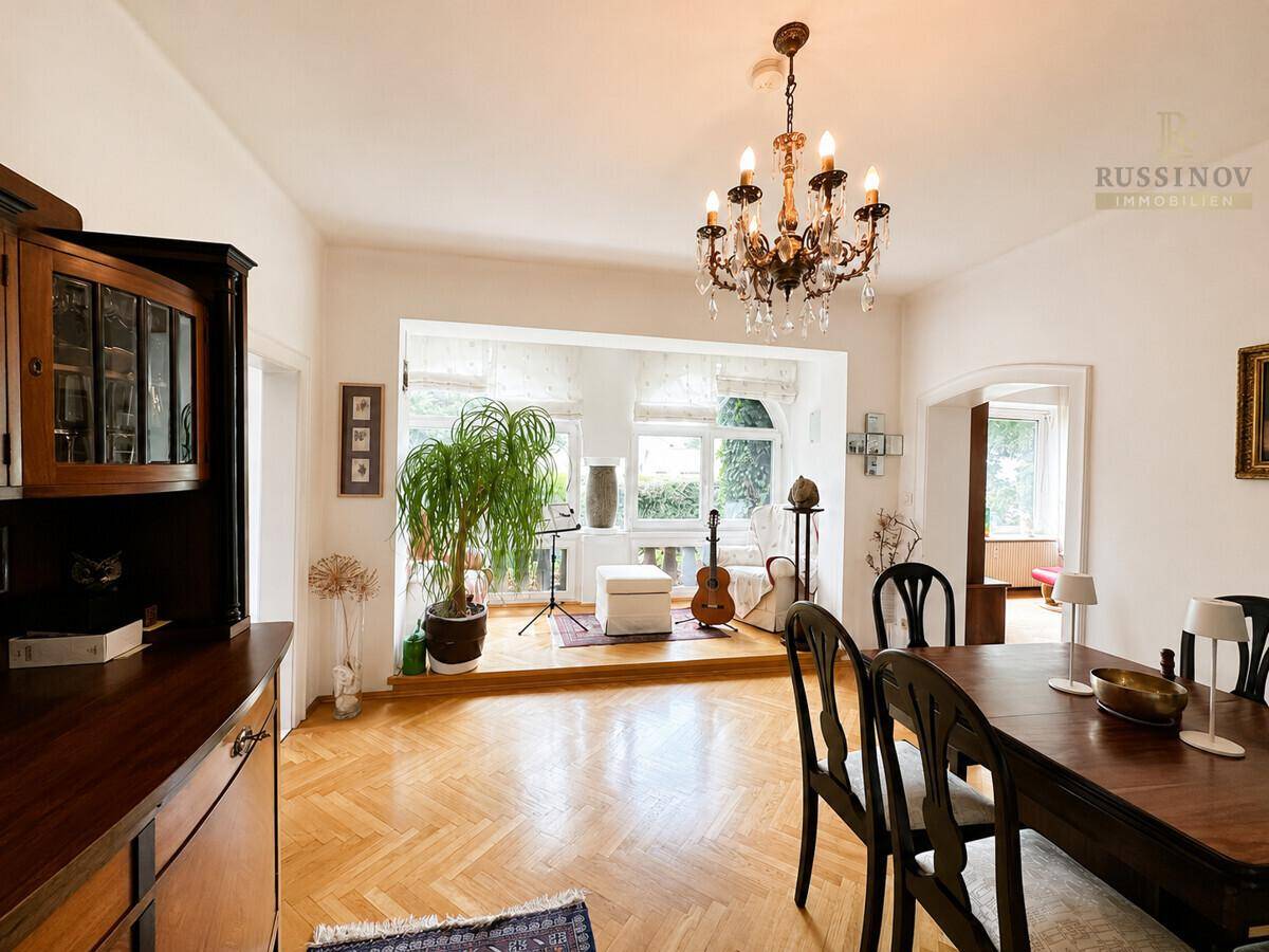 Heller Wohnbereich mit Parkettboden und großen Fenstern, ausgestattet mit Pflanzen und Musikinstrumenten.