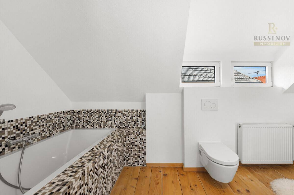 Modernes Badezimmer mit Badewanne, Wand-WC und Mosaikfliesen unter Dachschrägen.