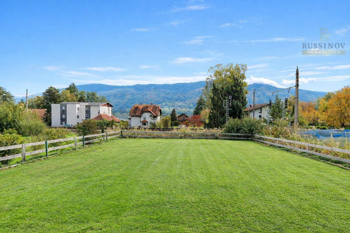 Weitläufige Rasenfläche mit Blick auf die umliegende Landschaft und ferne Berge unter blauem Himmel.