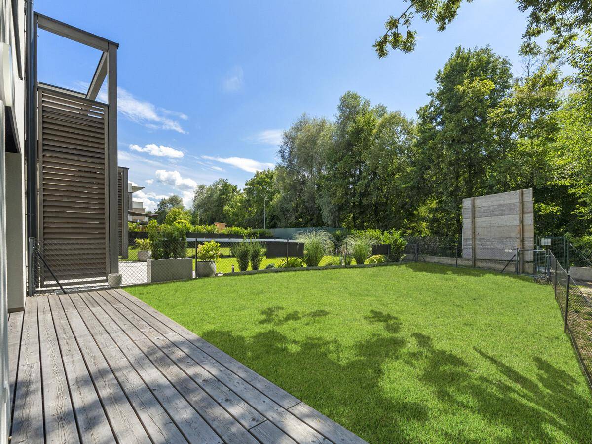 Geräumige Holzterrasse grenzt an einen gepflegten Rasenbereich mit üppiger Bepflanzung.