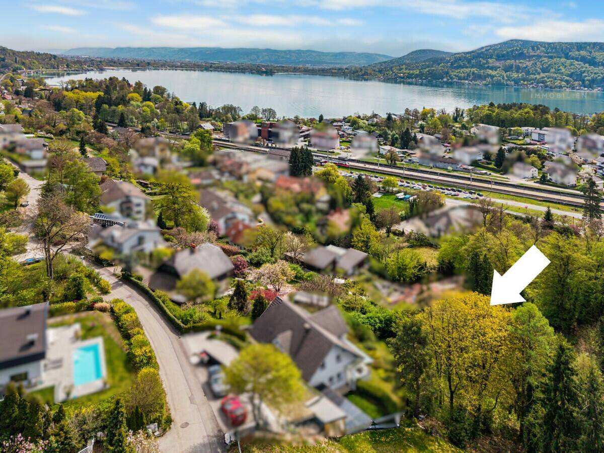 Luftaufnahme eines Wohngebiets mit See im Hintergrund und umliegender grüner Landschaft.