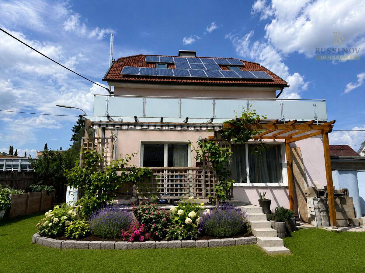 Rückseite des Hauses mit blühendem Garten, Terrasse und Solaranlage auf dem Dach.