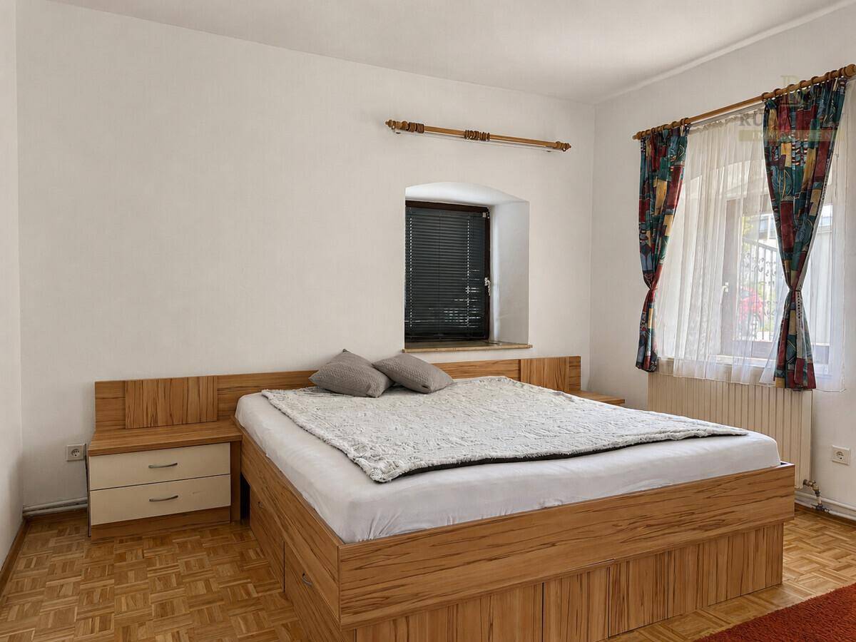 Gemütliches Schlafzimmer mit Holzbett, Nachttischen und Fenstern mit Vorhängen.