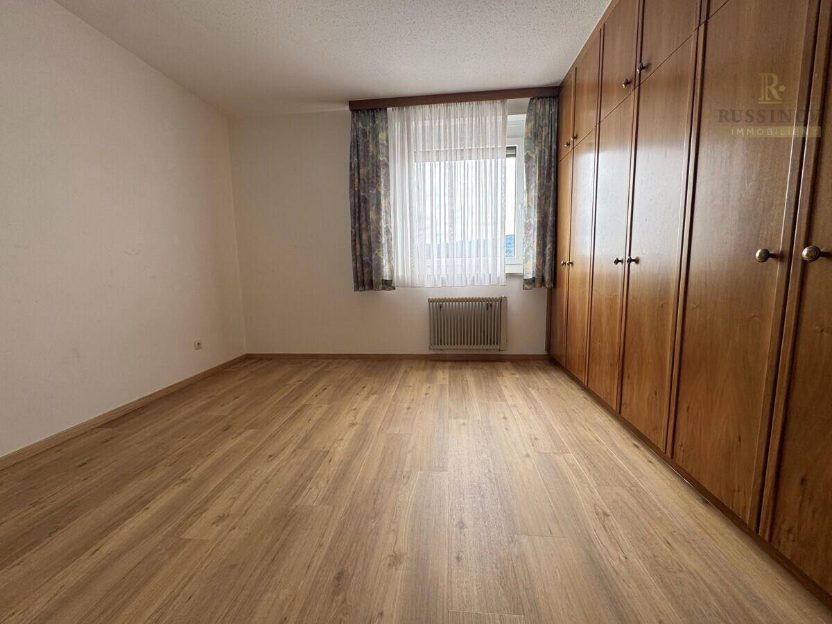 Schlafzimmer mit großem Einbauschrank, Laminatboden und Fenster mit Vorhängen.