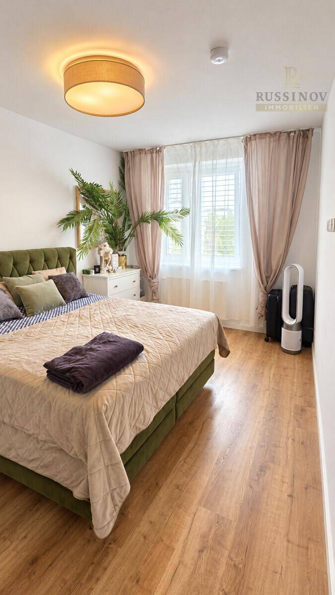 Gemütliches Schlafzimmer mit großem Bett, hellem Laminatboden und Fenster.