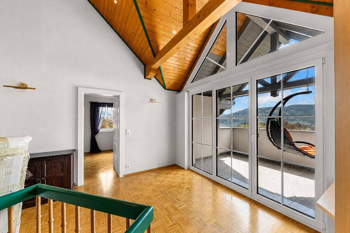 Lichtdurchfluteter Raum mit hohen Decken, Holzbalken und Zugang zu einem Balkon mit Aussicht.