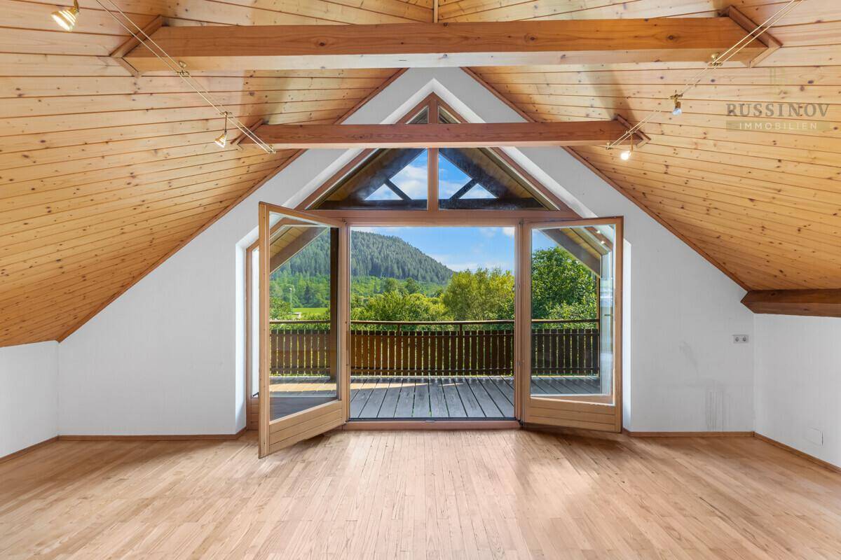 Helles Dachzimmer mit Holzbalken, hohen Decken und Zugang zu einem Balkon mit Bergblick.