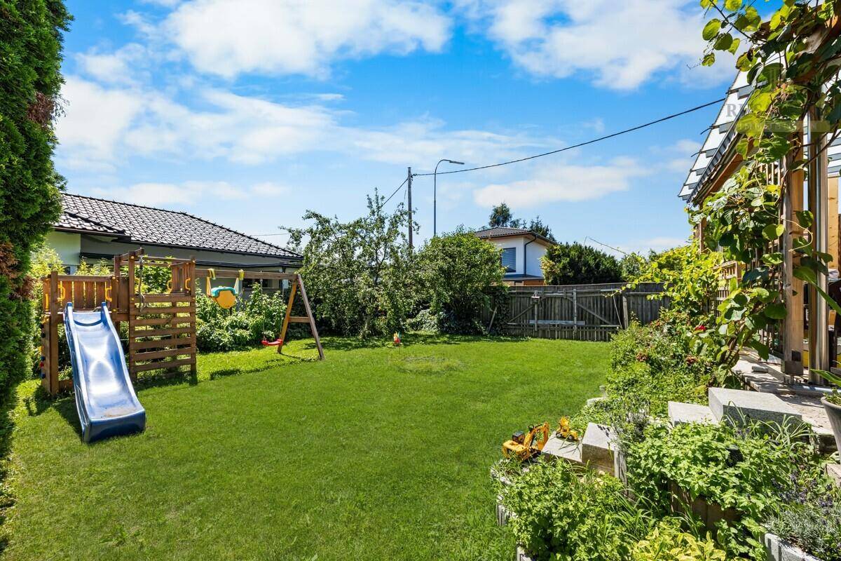 Gepflegter Garten mit großer Rasenfläche und einem Spielplatz, ideal für Familien mit Kindern.