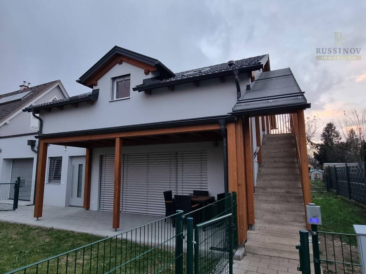 Überdachte Terrasse mit Sitzgelegenheiten und Außentreppe, die zum oberen Stockwerk führt.