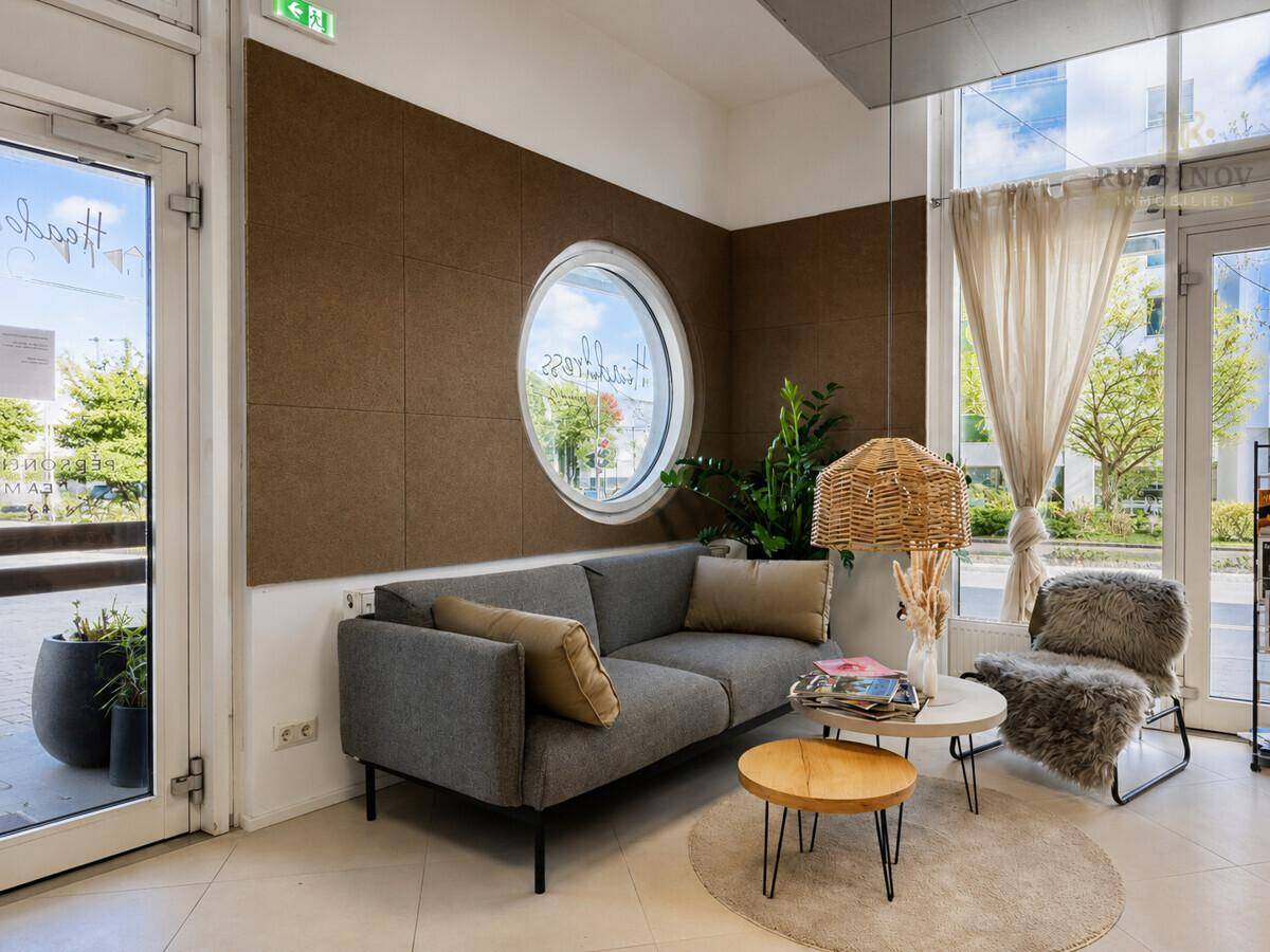 Gemütlicher Wartebereich mit modernem Sofa, runden Fenstern und dekorativer Beleuchtung, ideal für Gäste.