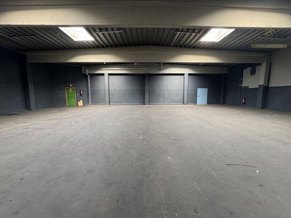 Großer, leerer Innenraum mit hohen Decken, Oberlichtern und Betonboden, ideal für Lager oder Werkstatt.