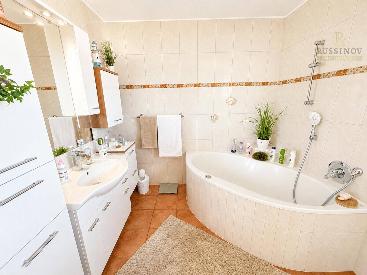 Badezimmer mit Badewanne, Doppelwaschbecken und beigen Fliesen.