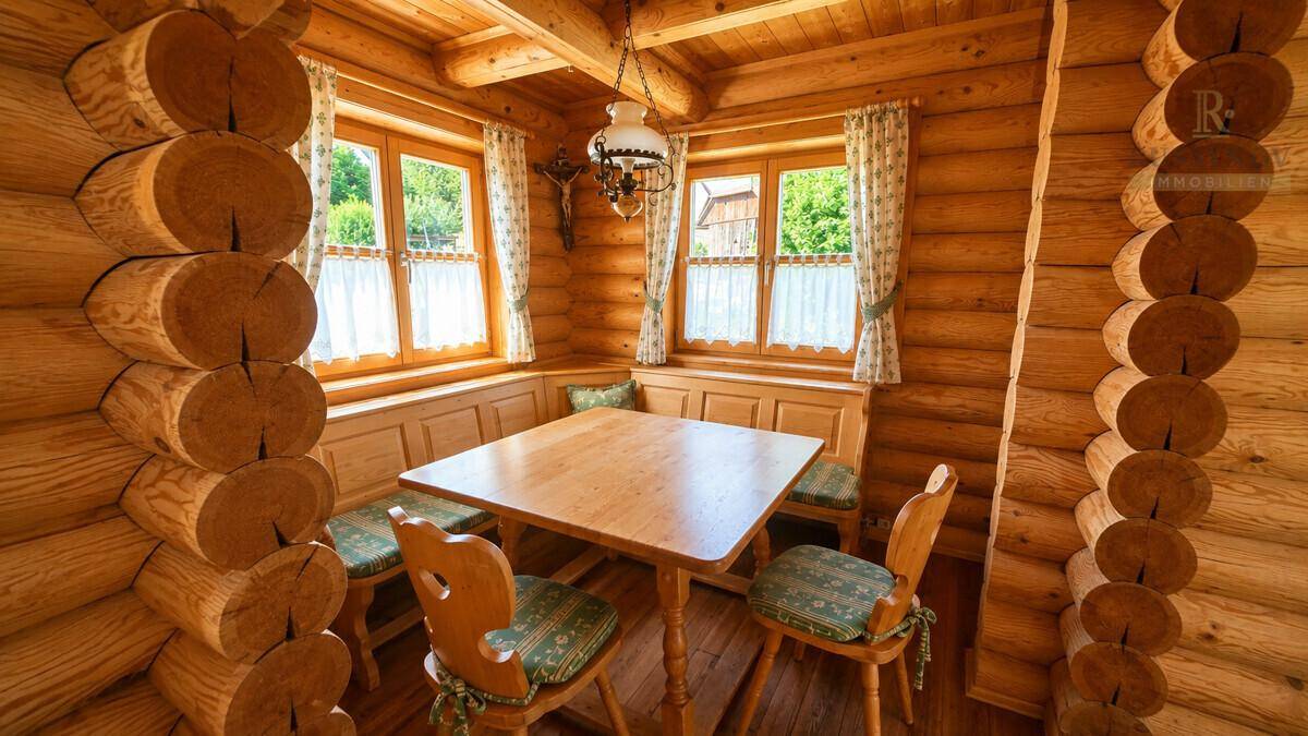 Gemütlicher Essbereich im Holzhaus mit traditionellen Möbeln und Fenstern mit Blick ins Grüne.