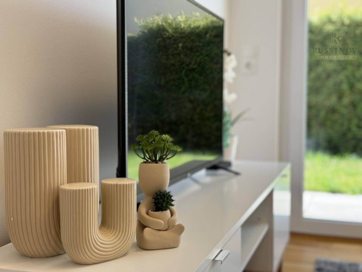 Detailansicht des Wohnzimmers mit TV-Möbel, Dekoration und Blick ins Grüne.