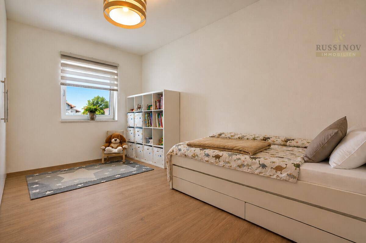 Kinderzimmer mit Einzelbett, weißem Regal und hellem Holzboden, ideal für junge Bewohner.