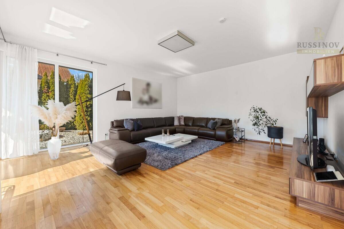 Geräumiges Wohnzimmer mit Parkettboden, großer Eckcouch und Zugang zum Garten.