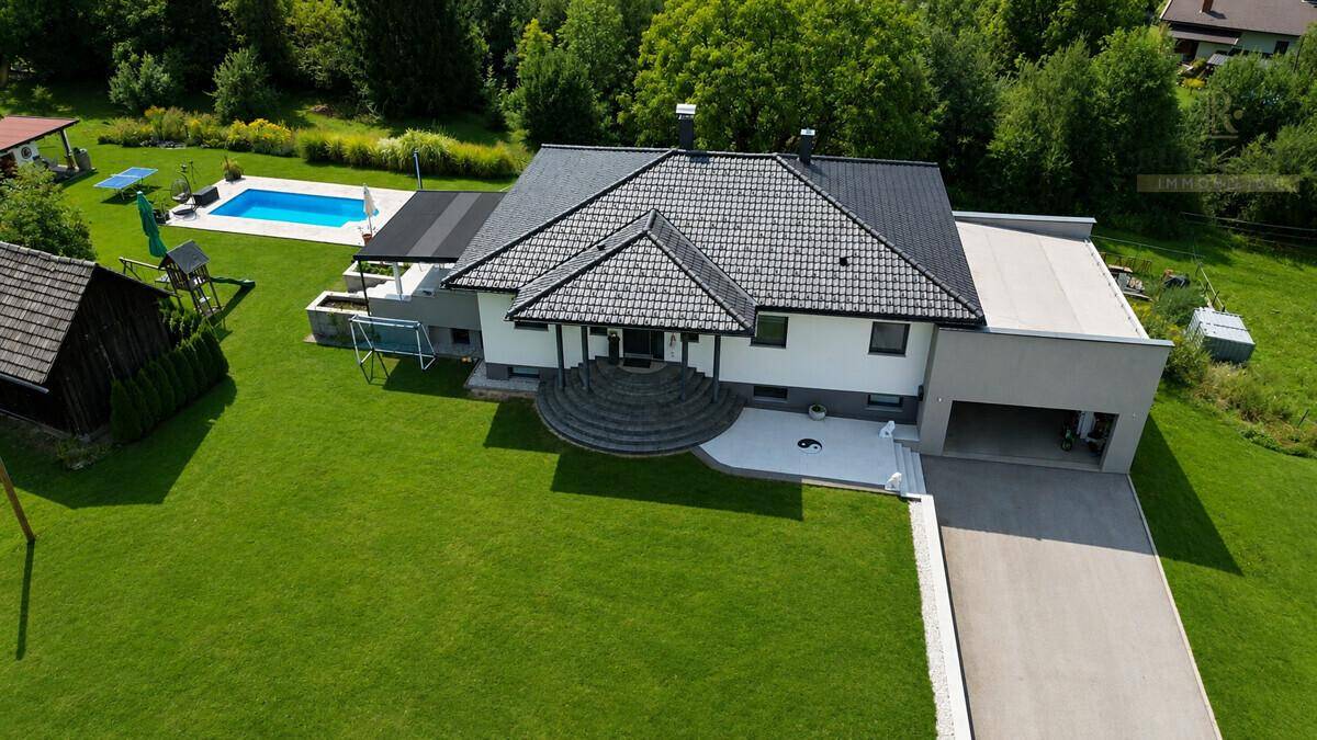 Luftaufnahme eines modernen Hauses mit großem Garten, Poolbereich und integrierter Garage.