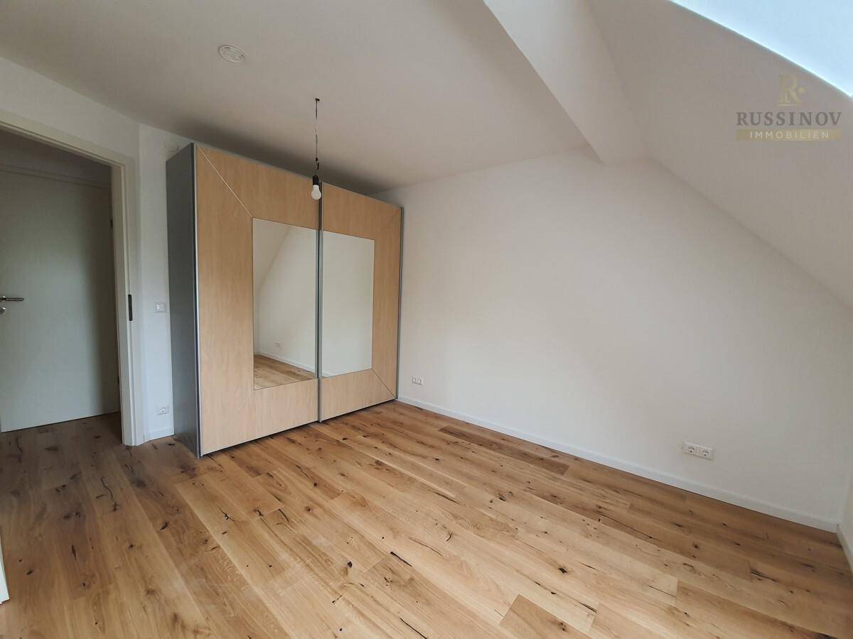 Schlafzimmer im Dachgeschoss mit Einbauschrank und hellem Holzboden.