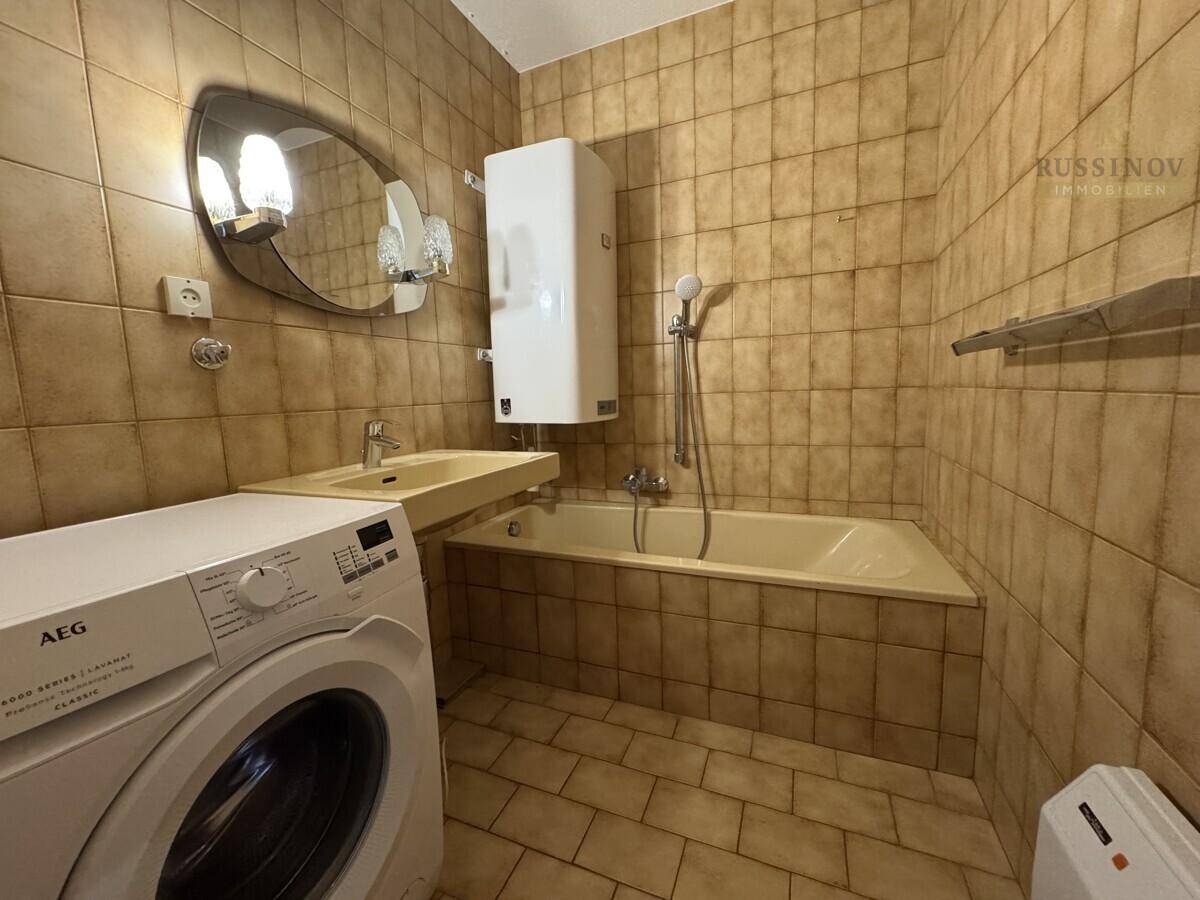 Gefliestes Badezimmer mit Badewanne, Waschbecken und Waschmaschine, in einem traditionellen Stil.