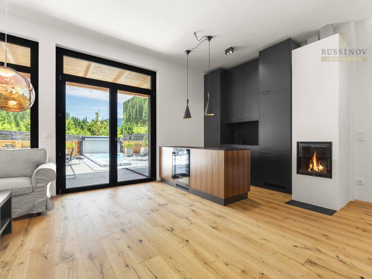 Moderner offener Wohnbereich mit schwarzer Küche, Holzboden, Kamin und Zugang zur Terrasse.