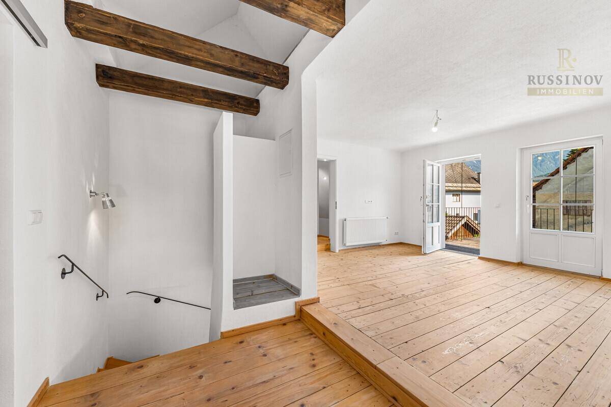 Heller Wohnbereich mit Holzboden, sichtbaren Balken und direktem Zugang zum Außenbalkon.