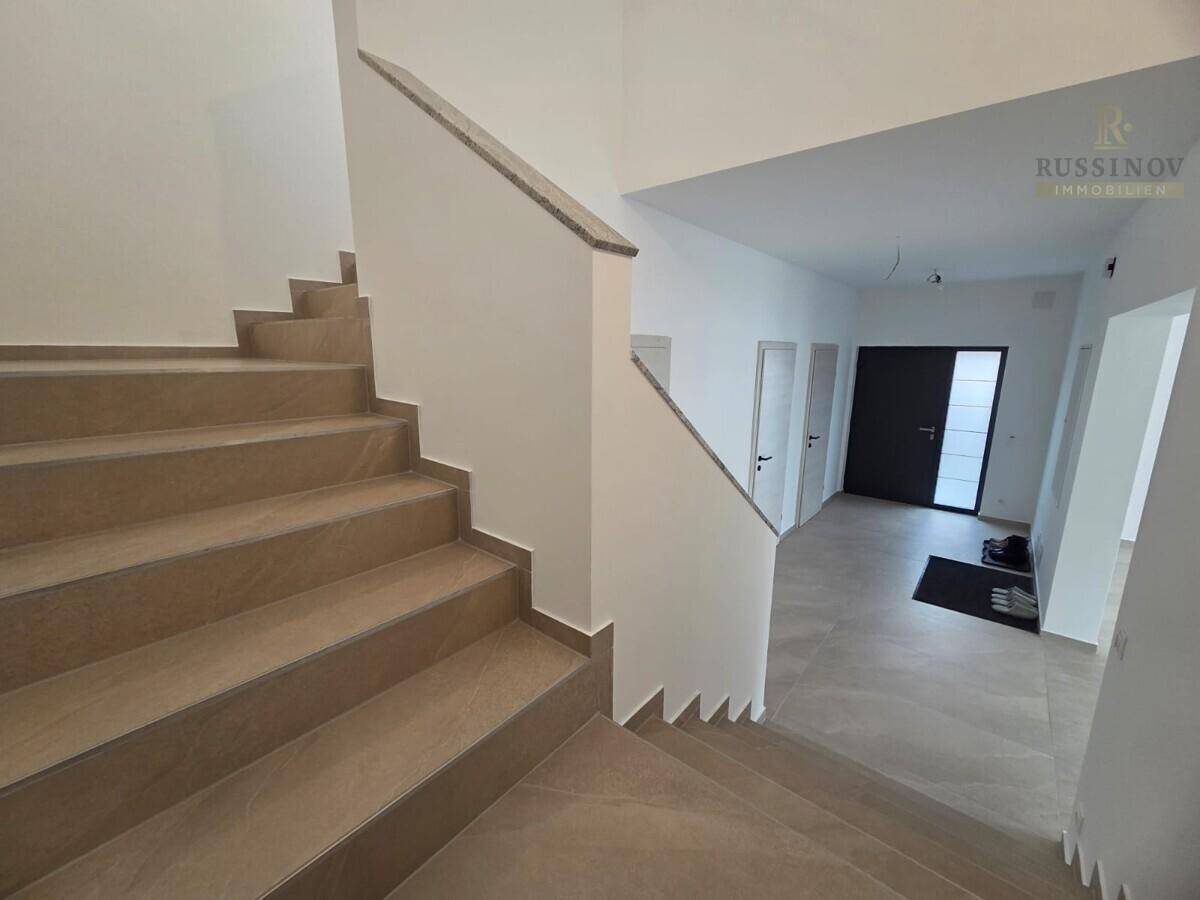 Heller Eingangsbereich mit moderner Treppe und Fliesenboden, der zu den oberen Etagen führt.